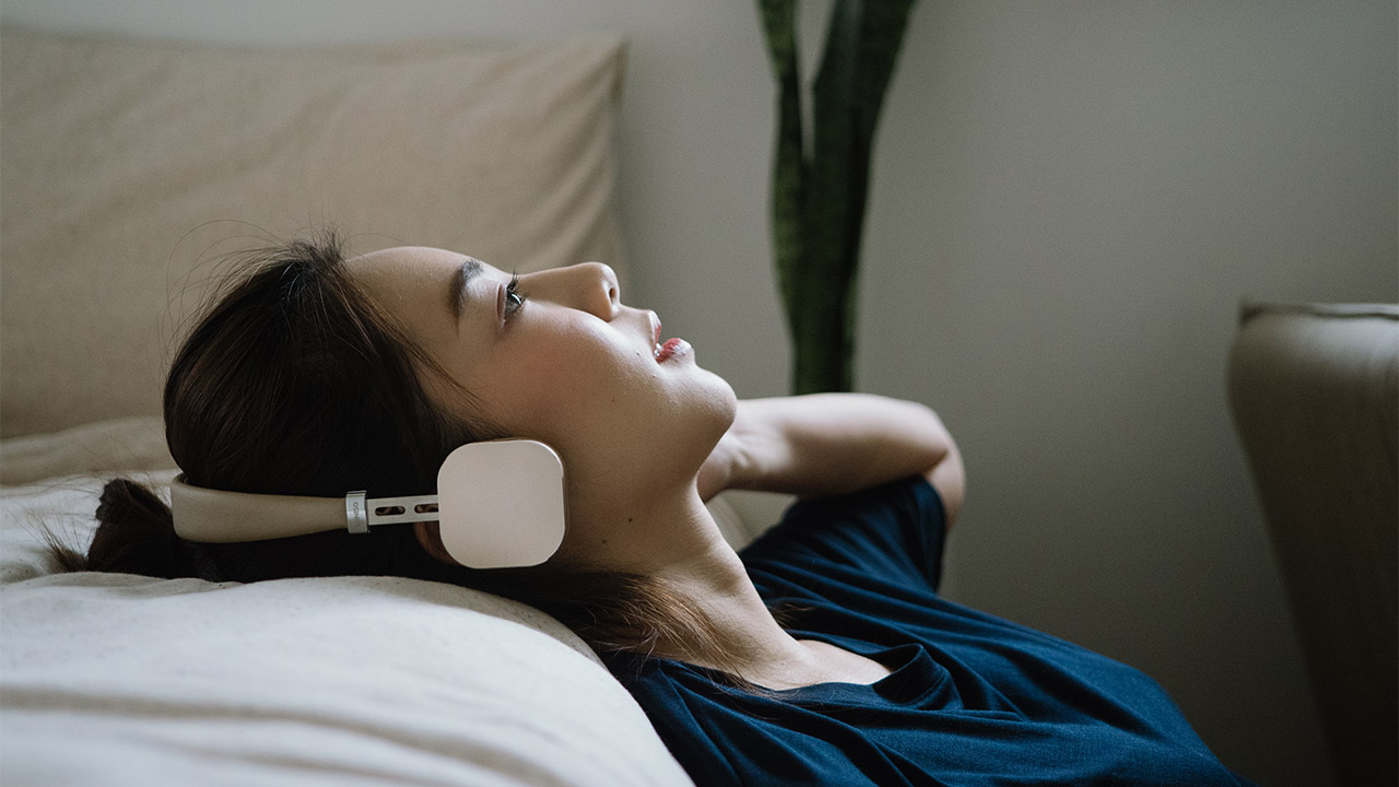 Photo of a woman with her head resting on a sofa, wearing headphones.
