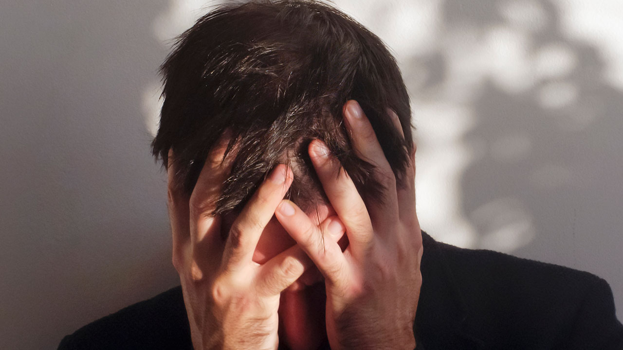 Photo of a person with their head in their hands, appearing frustrated.